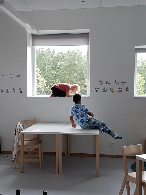 Två barn i ett klassrum. Det ena barnet sitter på ett bord och det andra är hopkrupet i fönsternischen.