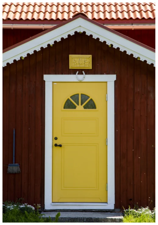 Foto på röd liten stuga med gul dörr.