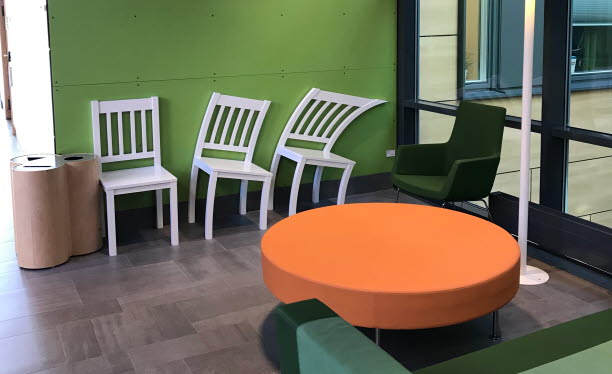 Grönt väntrum med vita stolar och orange bord.