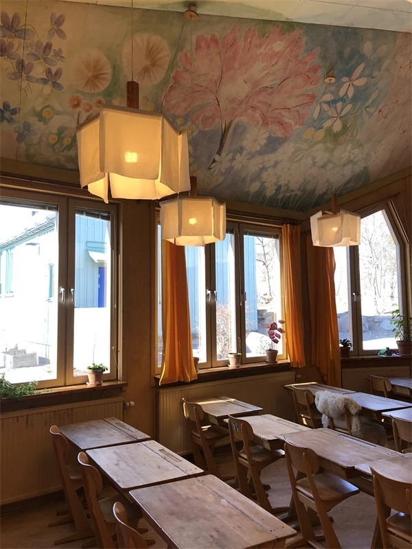 Takmålningen består av blommor i pastellfärjer, vita lampor av tyg hänger över skolbänkar i trä.