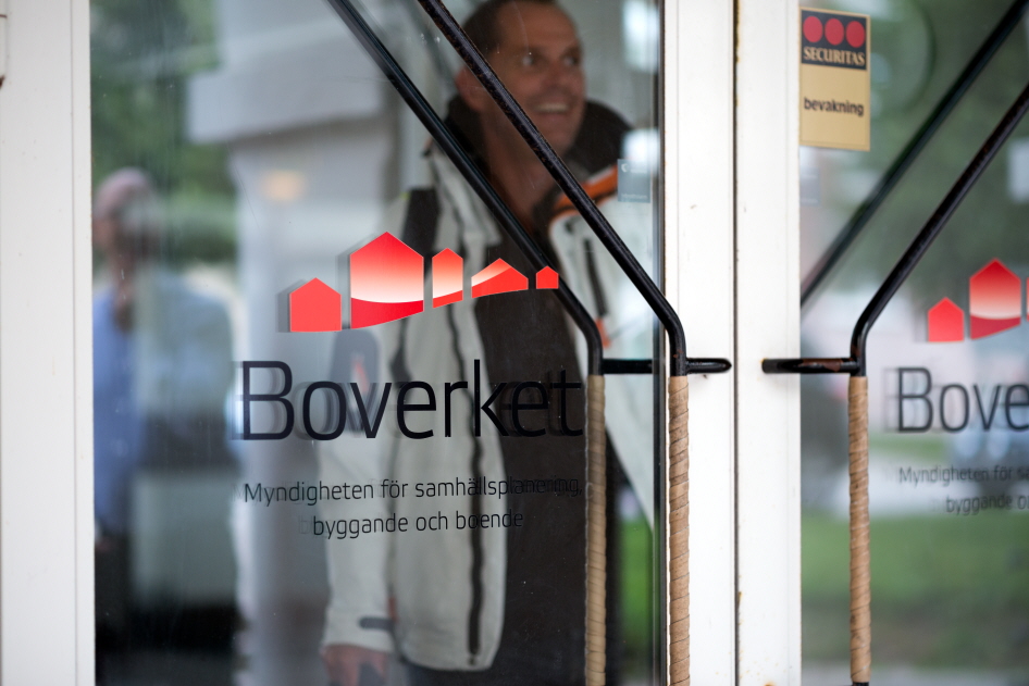 Dörrar in till Boverkets kontor i Karlskrona. Boverkets logotyp sitter på glasdörren. Reflektionen av en medarbetare syns i glaset.