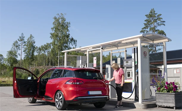 En person står och tankar en röd bil vid en pump.