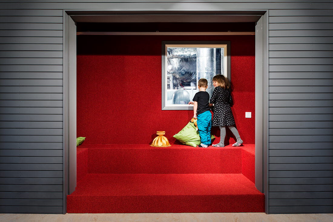 Interiör från Hedlunda förskola. Två barn står i röd trappa och kikar in i teknikrummet.