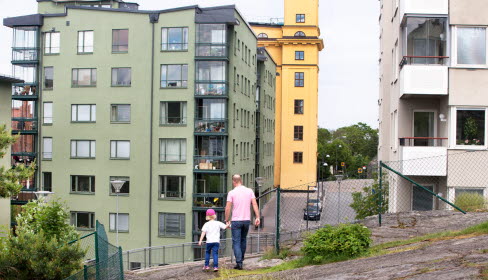 Man och barn hand i hand framför flerbostadshus. 