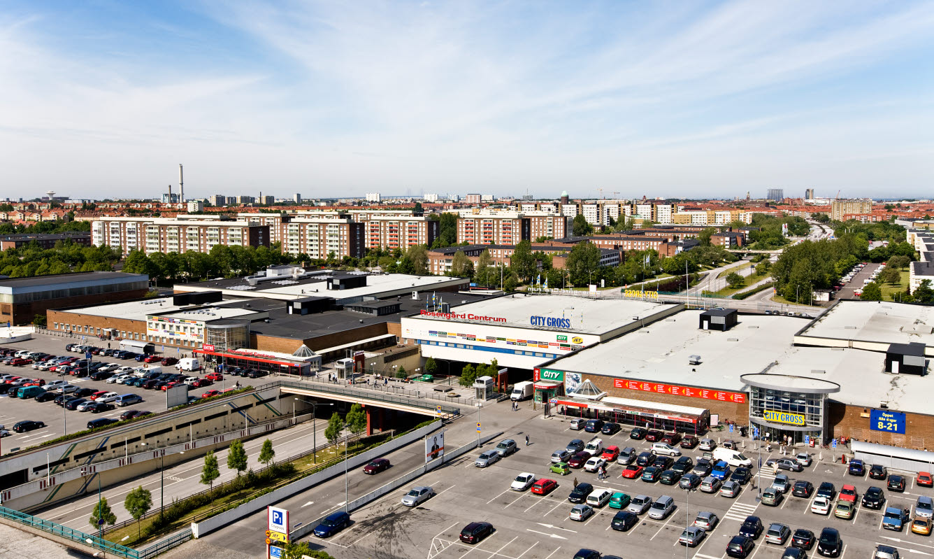 Flygbild över stadsmiljö med köpcentrum , viadukt samt flerfamiljshus . 