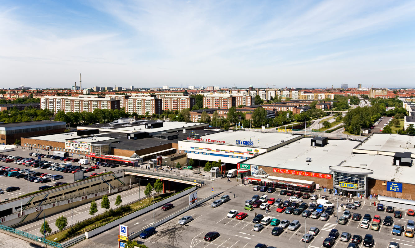 Flygbild över stadsmiljö med köpcentrum , viadukt samt flerfamiljshus .