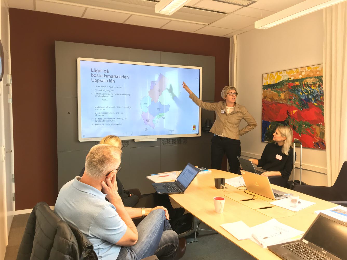 En kvinna pekar på en bild och informerar om bostadssituationen inför några åhörare.
