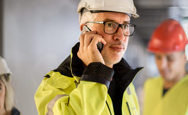 En man i varseljacka och arbetskläder talar i mobiltelefon. Foto: Scandinav/Plattform.