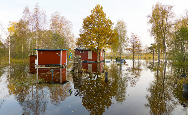 Foto på mindre byggnader i ett översvämmat grönområde.