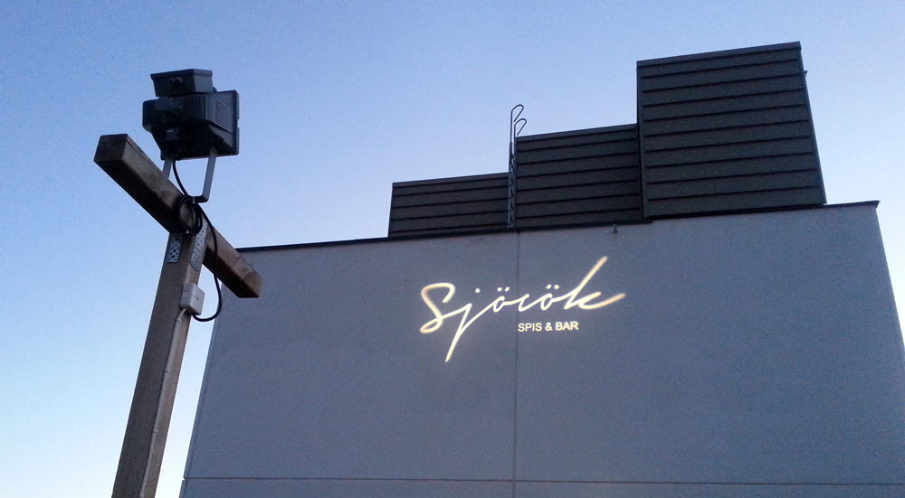 Foto på en ljusprojektion på en restaurangbyggnad med texten Sjörök spis & bar..