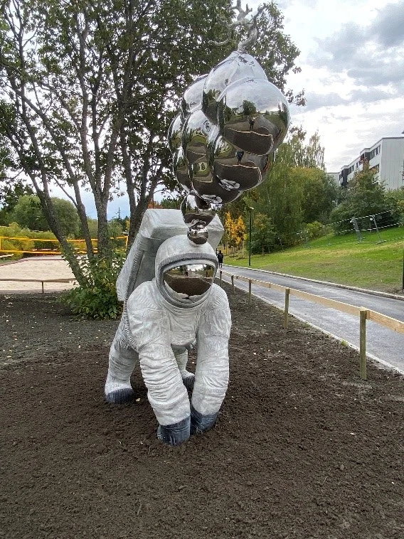 Skulptur i form av en astronaut som står i jorden och det kommer silverfärgade bubblor ut ur hjälmen