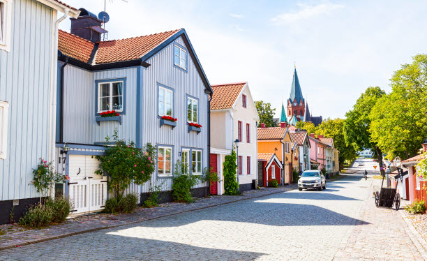 Trähus längsmed gata av kullersten. Kyrka och grönska i fonden.