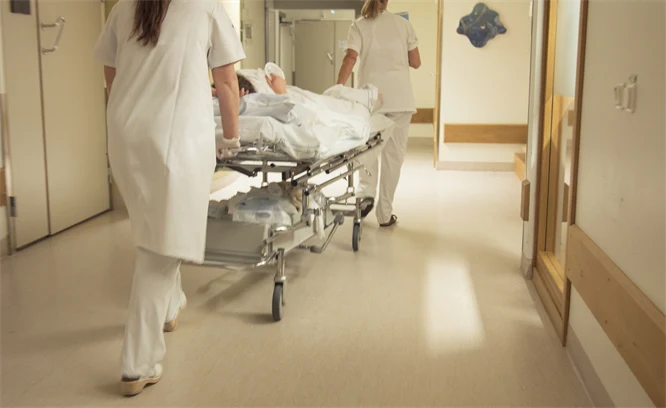 Två sjuksköterskor som rullar en bår med en patient på i en korridor.