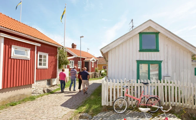 Fyra personer vandrar längs kullerstensgator i en kulturmiljö bland röda och vita trähus. Foto: Anders Järkendal/Scandinav