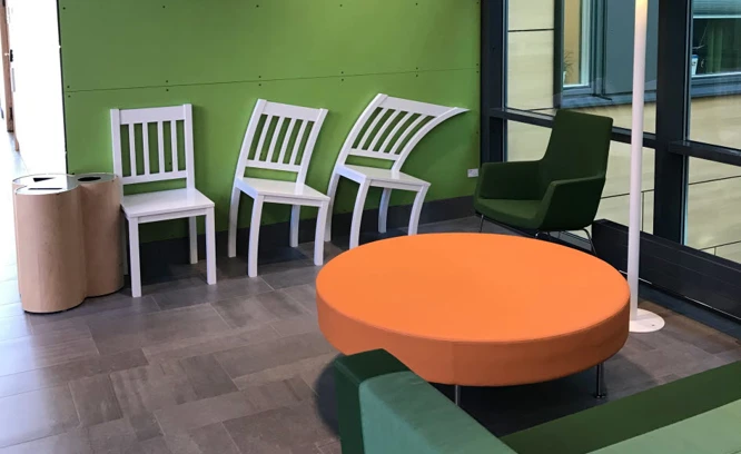 Grönt väntrum med vita stolar och orange bord.