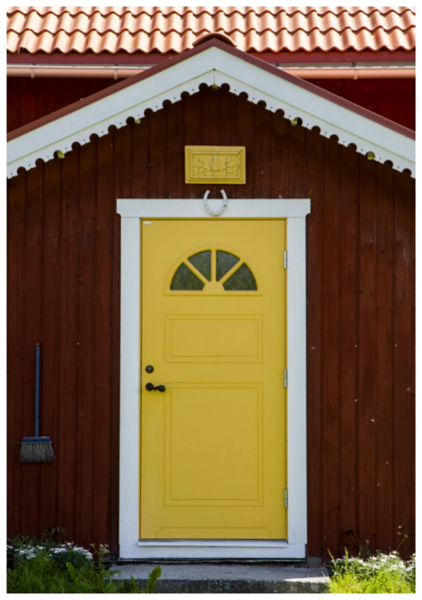 Foto på röd liten stuga med gul dörr.