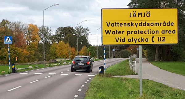 Varningsskylt för vattenskyddsområde. Skylten står vid en väg med övergångsställe.
