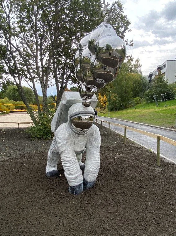Skulptur i form av en astronaut som står i jorden och det kommer silverfärgade bubblor ut ur hjälmen