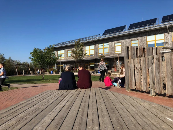 Vuxna människor som sitter på ett trädäck och blickar ut över skolgården.