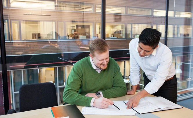 Två kollegor i ett konferensrum. Den enda står bredvid och hjälper den andra.