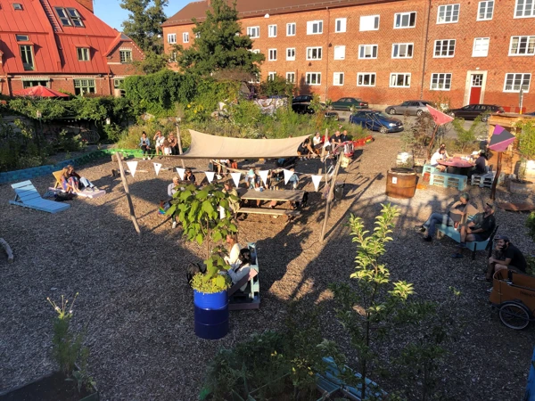 Foto som visar en innergård vid flerbostadshus med växter, solstolar och soltak.