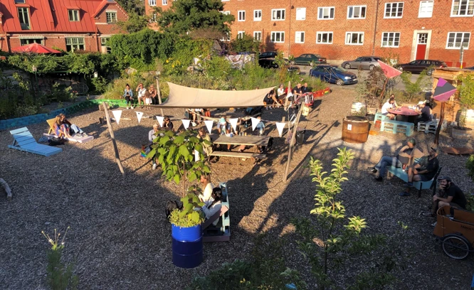 Foto som visar en innergård vid flerbostadshus med växter, solstolar och soltak.