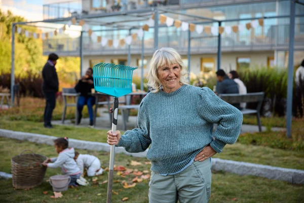 En person med en räfsa på en innergård i ett bostadsområde.