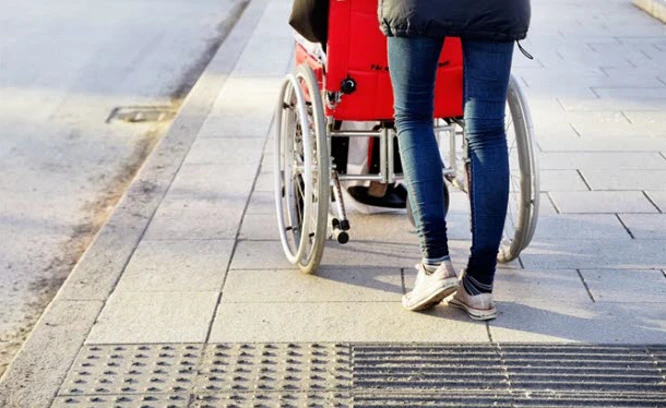 En jkvinna som kör en rullstol på en trottoar. Foto: Scandinav