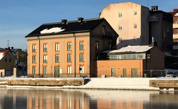 Några äldre putsade byggnader vid stranden speglar sig i en vattenyta med blank is