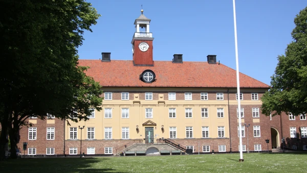 Stor tegelbyggnad i 4 våningar med klocktorn på taket.