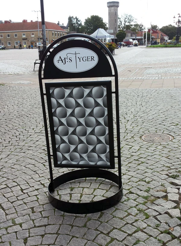 Foto på gatupratare i svart metall med ett grafiskt tyg och texten AJ:s Tyger stående på en gata..