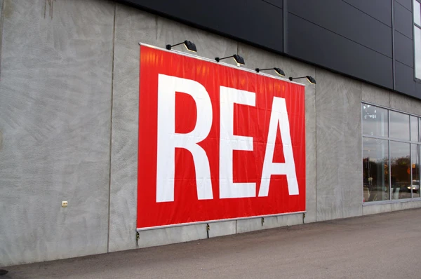 Foto av en röd vepa med vit text Rea på en husfasad.