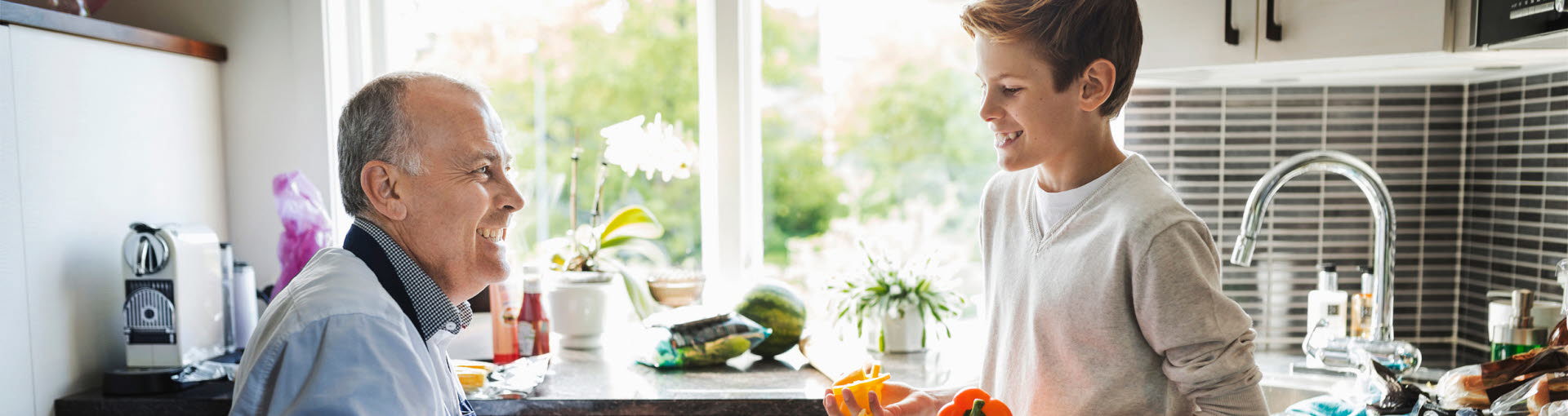 Pappa och son lagar mat i köket. Pappan använder rullstol. De är glada.